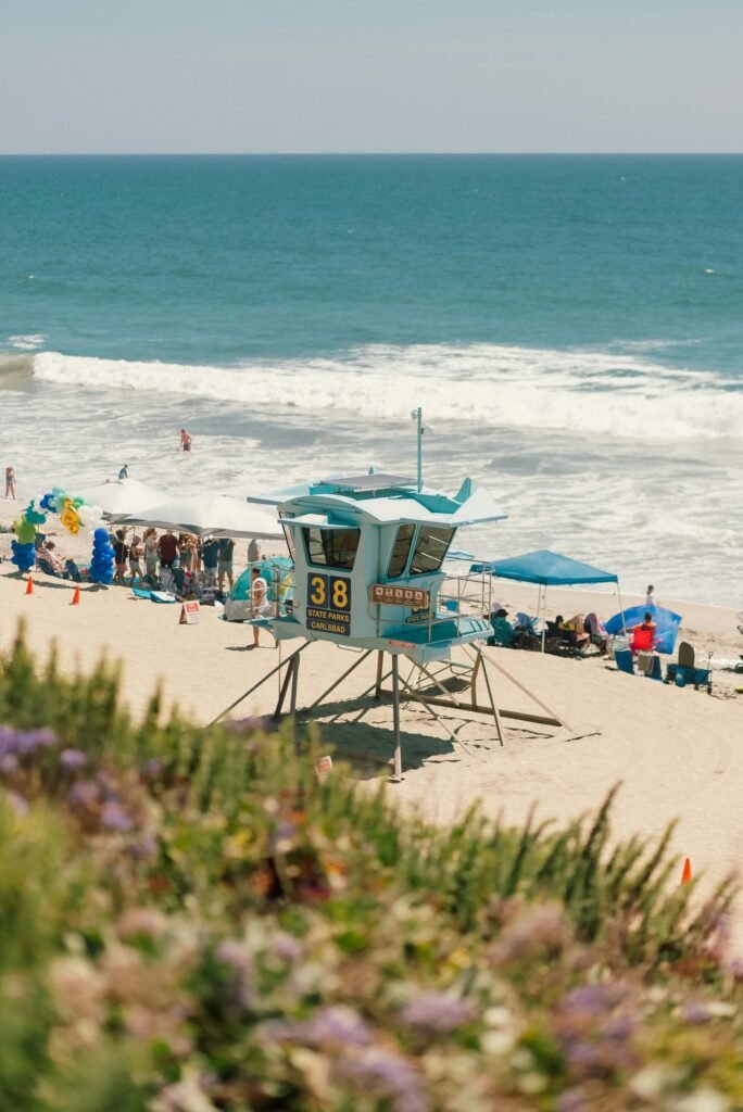 Lively beach scene with a lifeguard hut, tourists, and ocean waves under a clear sky.