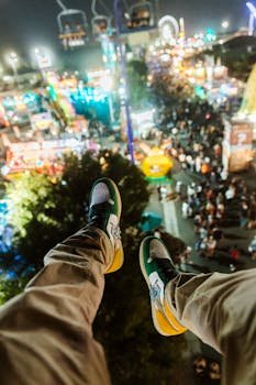 A thrilling personal perspective of an amusement park at night with vibrant lights and crowds below.